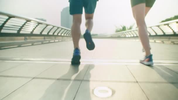 Sección baja seguir plano de piernas de pareja en ropa deportiva corriendo en pasarela urbana mientras hacen ejercicio juntos al aire libre en la ciudad - Imágenes, Vídeo