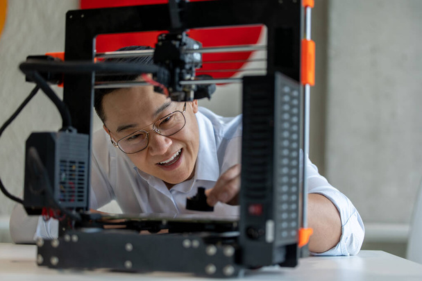 Asian male designer using 3D printer in office, working with new technology ideas. - Foto, Bild