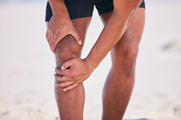 Handen, knie pijn en atleet op het strand, ongeval en fitness-oefening in sport workout outdoor. Benen, verwondingen en artritis bij de mens, spierproblemen en fibromyalgie bij medische noodgevallen voor osteoporose. - Foto, afbeelding