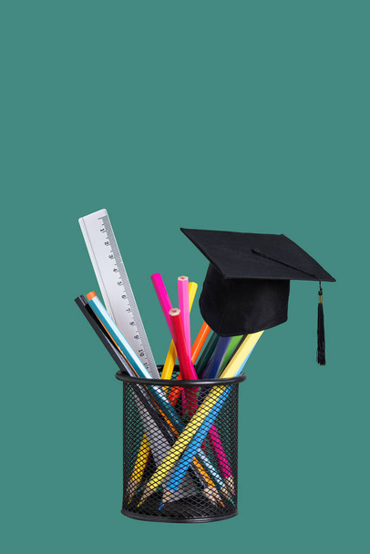 Desk organizer with colourful pencils and academic cap on green background. Pencil Holder with school supplies. Back to school concept. - Photo, Image