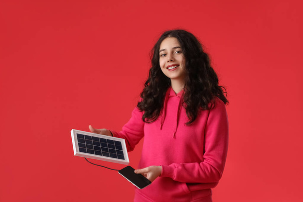 Teini tyttö kannettava aurinkopaneeli lataus matkapuhelin punaisella taustalla - Valokuva, kuva