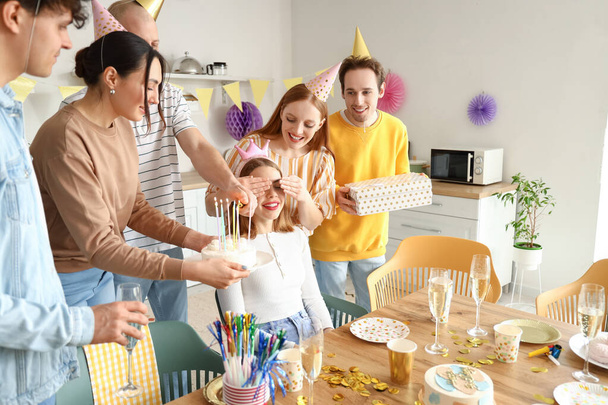 Νεαρή γυναίκα φέρνει τούρτα γενεθλίων στη φίλη της στο πάρτι. - Φωτογραφία, εικόνα