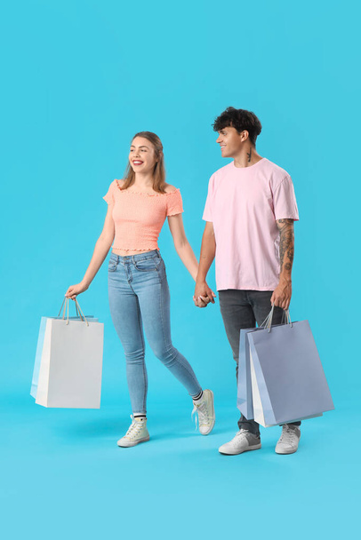Alışveriş torbalarıyla mavi arka planda yürüyen mutlu genç çift. - Fotoğraf, Görsel
