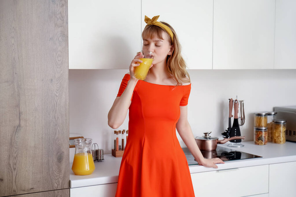 Jeune femme buvant du jus d'orange dans la cuisine
 - Photo, image
