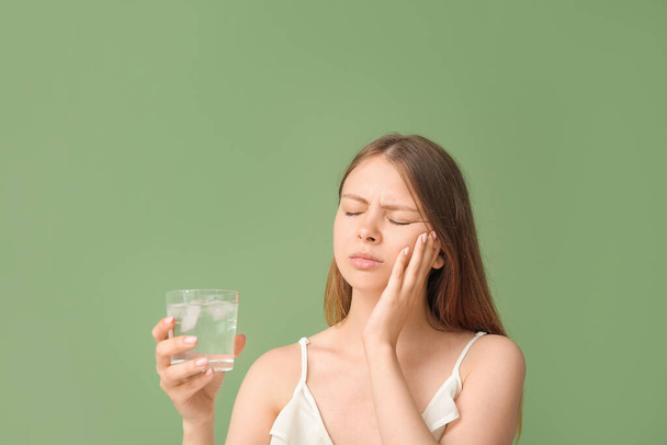 Молода жінка з чутливими зубами і склянкою холодної води на зеленому фоні - Фото, зображення