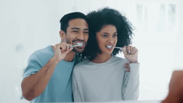 Onnellinen pari, hampaiden harjaus ja peili aamulla rutiini, hammashygienia tai hoito kylpyhuoneessa kotona. Rotujenvälinen mies ja nainen puhdistus suun, suun tai ikenien onnea tai hampaiden valkaisuun yhdessä. - Materiaali, video