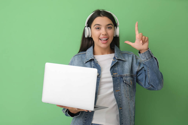 Happy female programmer in headphones with laptop pointing at something on green background - Foto, Imagem