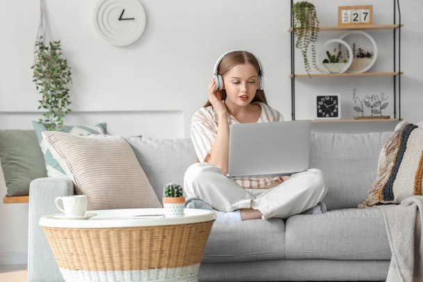 Jeune femme dans les écouteurs travaillant avec un ordinateur portable à la maison - Photo, image