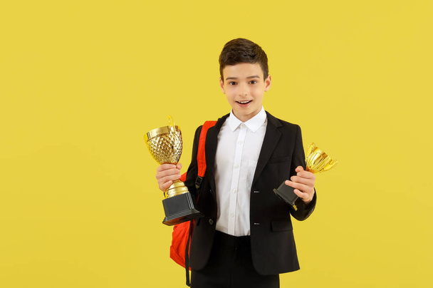 Okos kis iskolás fiú díjnyertes csésze sárga háttér - Fotó, kép