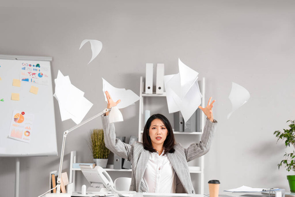 gestresste aziatische zakenvrouw zitten aan tafel en gooien papier in kantoor - Foto, afbeelding