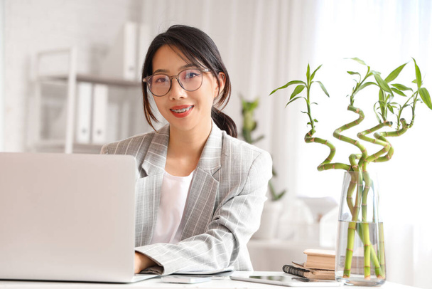 Junge asiatische Geschäftsfrau sitzt am Tisch und arbeitet im Büro mit Laptop - Foto, Bild