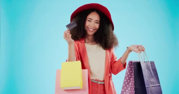 Gezicht, vrouw en een creditcard voor winkelen op een blauwe achtergrond en enthousiast over retail tassen. Gelukkig, cadeau en portret van een meisje met een glimlach van mode korting, betaling en een kledingverkoop. - Video