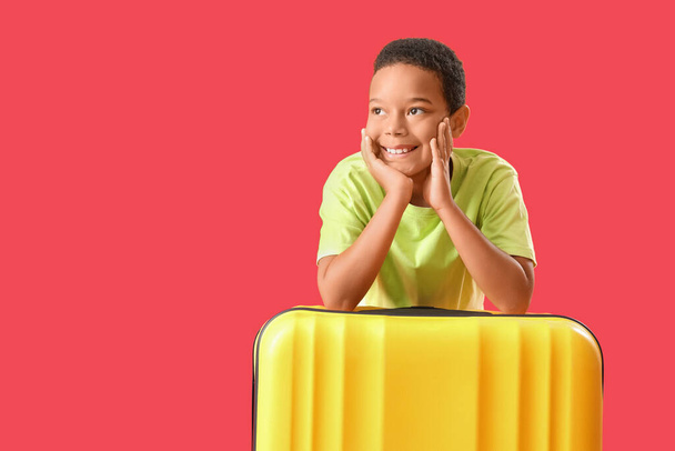 Pequeño niño afroamericano con maleta sobre fondo rojo - Foto, Imagen