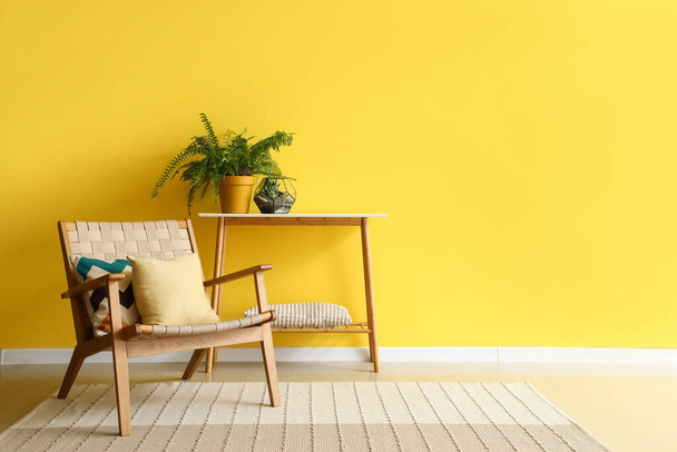 Poltrona elegante e planta de sala na mesa de console perto da parede amarela - Foto, Imagem