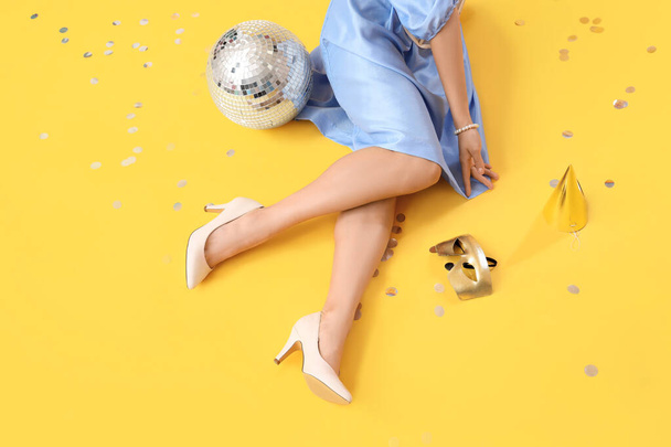 Beine der modischen schönen jungen Frau mit Discokugel auf gelbem Hintergrund - Foto, Bild