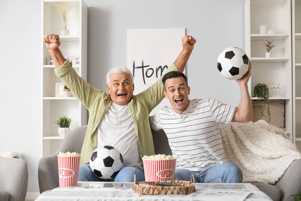 Šťastný mladý muž se svým otcem sledovat fotbal doma - Fotografie, Obrázek