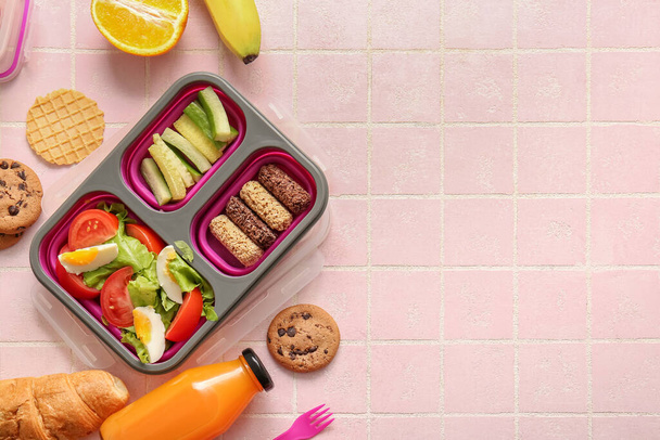 Scatole da pranzo con cibo delizioso e bottiglia di succo su sfondo di piastrelle rosa - Foto, immagini