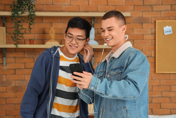 Άνδρες φοιτητές με ακουστικά που χρησιμοποιούν κινητό τηλέφωνο σε dorm room - Φωτογραφία, εικόνα