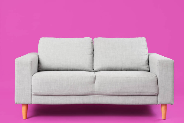 ピンクの背景に居心地の良い灰色のソファー - 写真・画像