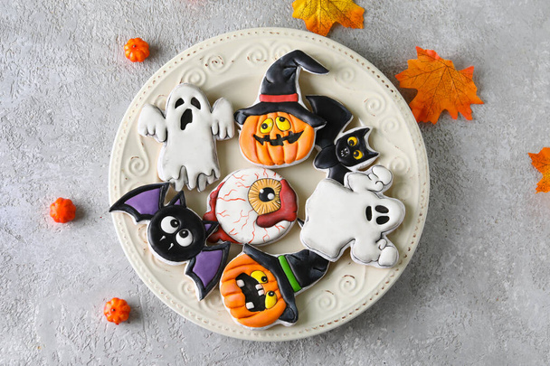Piatto con gustosi biscotti, zucche e foglie secche per la celebrazione di Halloween su sfondo grigio - Foto, immagini