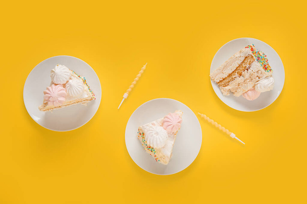 Platos con trozos de delicioso pastel de cumpleaños y velas sobre fondo amarillo - Foto, Imagen