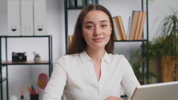 Portrét šťastně se usmívající brunetky Kavkazská podnikatelka na domácí kancelářský stůl se odvrátí pohledem upřeným na kameru. Žena ve formální košili. Hezká dívka vzdálený online pracuje na notebooku - Záběry, video