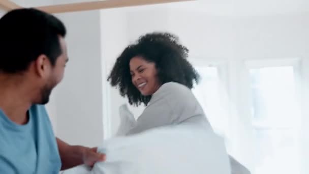 Happy couple, bed and playing pillow fight in fun morning, wake up or bonding together at home. Interracial man and woman smile in happiness for weekend, holiday or break with cushion in bedroom. - Footage, Video