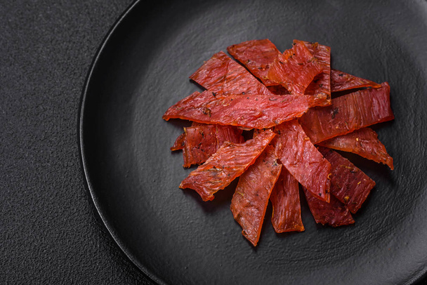 Delicious dried veal or turkey jerky with salt, spices and herbs on a dark concrete background - Foto, immagini