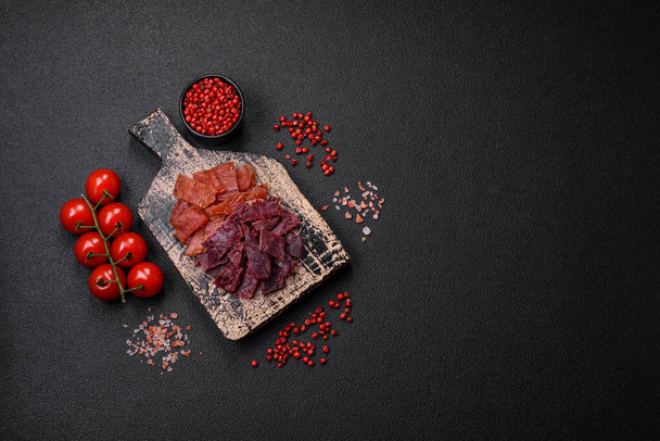 Köstliches getrocknetes Kalbfleisch oder Truthahn mit Salz, Gewürzen und Kräutern auf dunklem Betongrund - Foto, Bild