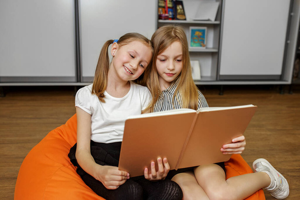 Πίσω στο σχολείο. Δύο χαρούμενα κορίτσια διαβάζουν βιβλία και μιλάνε στο σπίτι. Φιλία, οικογένεια, παιδική ηλικία και σπουδές. - Φωτογραφία, εικόνα