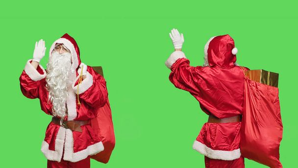 Sorridente Babbo Natale saluta le persone sulla macchina fotografica, salutando e agitando allegro sentimento felice diffondere spirito di festa. Babbo Natale con sacchetto pieno di scatole regalo che celebrano l'evento invernale stagionale. - Foto, immagini