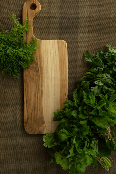 Bunches of fresh herbs, a wooden cutting board. Table top view. Mint, parsley, dill, coriander. Food background. Nutrition, greens, cooking, organic concept. Mock up. Copy space. Nobody - Photo, Image
