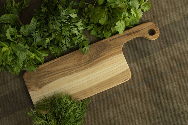Bunches of fresh herbs, a wooden board on a brown tablecloth. Top view. Mint, parsley, dill, coriander. Food background. Nutrition, greens, cooking, organic concept. Mock up. Copy space. Nobody - Photo, Image