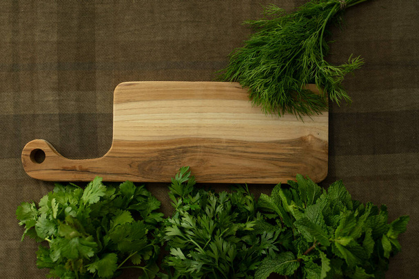 Bunches of fresh herbs, a wooden board on a brown tablecloth. Top view. Mint, parsley, dill, coriander. Food background. Nutrition, greens, cooking, organic concept. Mock up. Copy space. Nobody - Photo, Image