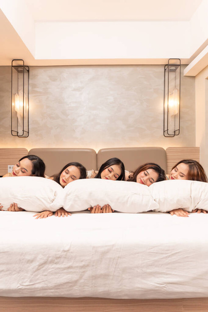 un grupo de mujeres asiáticas están durmiendo y apoyadas en almohadas blancas con sus amigos en un hotel de lujo por la noche - Foto, imagen