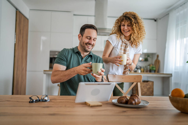 Young couple caucasian man and woman husband and wife enjoy cup of tea or coffee in the morning at home happy smile daily morning routine real people - Photo, Image