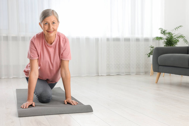 Senior woman in sportswear stretching on fitness mat at home, space for text - Foto, Imagen