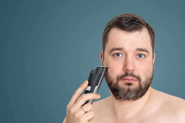 незахищений молодий чоловік ідеальної шкіри тримає електричну бритву гоління, ізольовано. Концепція косметичних процедур по догляду за шкірою. Вирощування для сучасної людини. красивий чоловік використовує електричну бритву - Фото, зображення