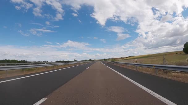 Empty highway road through the fields outside the city during sunny day. Two way asphalt road with country views with scattered and low clouds at Spain. Traffic ways transportation logistics concept. - Séquence, vidéo