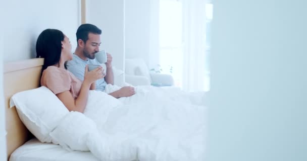 Αγάπη, πρωί και ένα ζευγάρι πίνοντας καφέ στο υπνοδωμάτιο μαζί, ενώ στο σπίτι τους για να χαλαρώσετε σε ένα Σαββατοκύριακο. Τσάι, χαμόγελο ή ευτυχία με έναν άντρα και μια γυναίκα να μιλάνε σε ένα κρεβάτι στο διαμέρισμά τους για ρομαντισμό. - Πλάνα, βίντεο