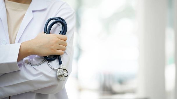 Cropped shot of an unrecognizable doctor standing with arms folded isolated on clear white hopital hall background. Copy space. medicine doctor holding stethoscope in hand wearing medical gown - Photo, Image