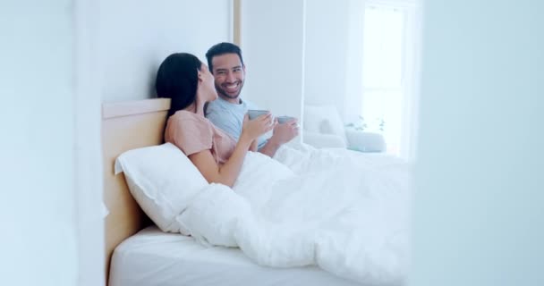 Love, morning and a couple drinking tea in bed together while in their home to relax on a weekend. Coffee, smile or happy with a man and woman talking in the bedroom of their apartment for romance. - Footage, Video