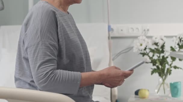 Inclinazione fino colpo di sorridente matura donna asiatica seduta sul letto d'ospedale e sms su smartphone - Filmati, video
