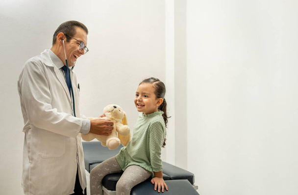 doctor using stethoscope listening teddy bear heartbeat. pediatrician building confidence on child. medic and kid smiling at doctor's office  - Photo, Image