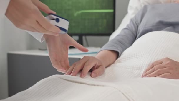 Unerkennbare Krankenschwester legt Finger-Pulsoximeter auf Patientin, die im Krankenhausbett liegt, um Sauerstoffsättigung zu überprüfen - Filmmaterial, Video