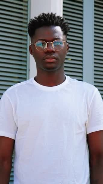 Portrait vertical de jeune Afro-Américain sérieux confiant regardant la caméra avec les bras croisés debout à l'extérieur. bel homme étudiant posant avec une attitude calme et coûteuse sur le campus universitaire - Séquence, vidéo