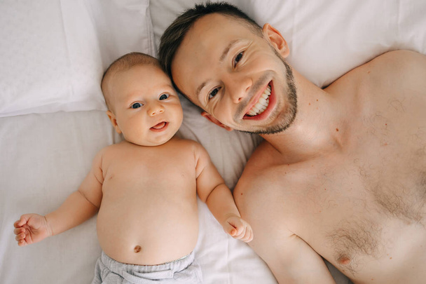 Young father with cute little son lying on bed, look at camera in bedroom. smiling top view. - Photo, Image