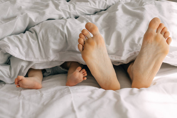 ребенок и отец ноги по утрам смотрят с одеяла - Фото, изображение