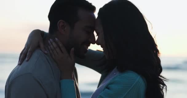 Love, sunset and kiss with couple at beach for relax, summer vacation and travel. Happy, adventure and wellness with man and woman hugging on seaside date for holiday, marriage and peace together. - Footage, Video