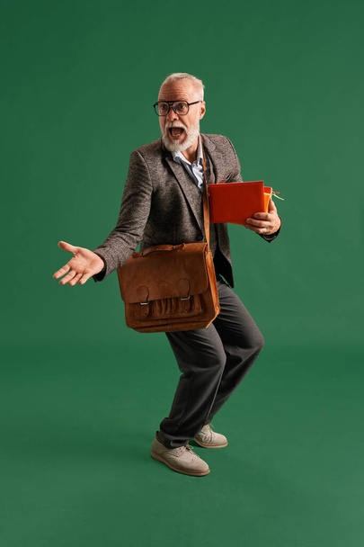 Full length portrait of senior man with beard in glasses, teacher wearing vintage suit with stack of books and brown business bag looks surprised. Concept of fashion, emotions, retro. Ad. - Photo, Image